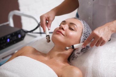 Mutlu olgun kadın güzellik salonunda mikro akım cilt bakımı yapıyor.