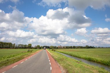 Hollanda 'da her iki tarafında kırmızı bisiklet yolu, perspektif, yoğun bulutlu gökyüzü altında ve yeşil çayırlar arasında, yolun sonunda tarım aracı sürücüler