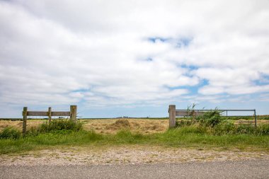 Tarım arazisinde açık olan çit kapısı, yüksek gökyüzü bulutlu, parlak yeşil çayır ve arka planda açık ufuk..
