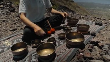Tibedt çalan genç bir Asyalı doğadaki bir dağda bakır bardaklar söylüyor.