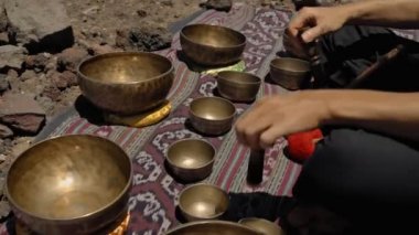 Tibedt çalan genç bir Asyalı doğadaki bir dağda bakır bardaklar söylüyor.