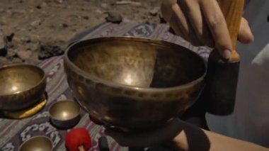 Tibedt çalan genç bir Asyalı doğadaki bir dağda bakır bardaklar söylüyor.