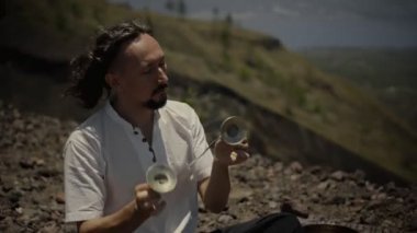 Tibedt çalan genç bir Asyalı doğadaki bir dağda bakır bardaklar söylüyor.