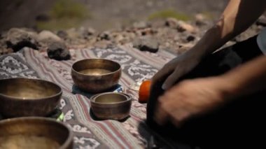 Tibedt çalan genç bir Asyalı doğadaki bir dağda bakır bardaklar söylüyor.