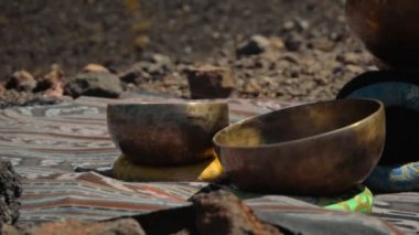 Tibedt çalan genç bir Asyalı doğadaki bir dağda bakır bardaklar söylüyor.