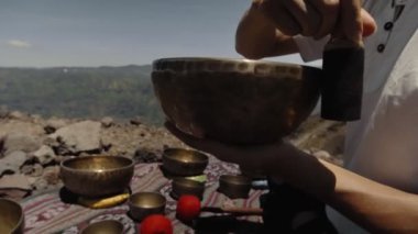 Tibedt çalan genç bir Asyalı doğadaki bir dağda bakır bardaklar söylüyor.
