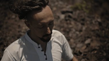 Tibedt çalan genç bir Asyalı doğadaki bir dağda bakır bardaklar söylüyor.