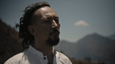 Tibedt çalan genç bir Asyalı doğadaki bir dağda bakır bardaklar söylüyor.