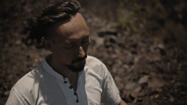 Tibedt çalan genç bir Asyalı doğadaki bir dağda bakır bardaklar söylüyor.