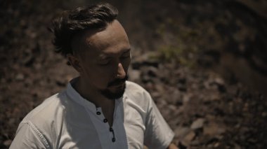 Tibedt çalan genç bir Asyalı doğadaki bir dağda bakır bardaklar söylüyor.