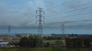 Gün batımında yeşil pirinç tarlasında yeni inşa edilmiş bir elektrik iletim kulesinin hava aracı görüntüsü.