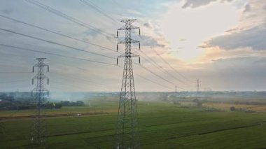 Gün batımında yeşil pirinç tarlasında yeni inşa edilmiş bir elektrik iletim kulesinin hava aracı görüntüsü.