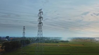 Gün batımında yeşil pirinç tarlasında yeni inşa edilmiş bir elektrik iletim kulesinin hava aracı görüntüsü.