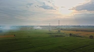 Gün batımında yeşil pirinç tarlasında yeni inşa edilmiş bir elektrik iletim kulesinin hava aracı görüntüsü.