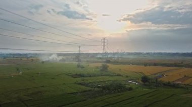 Gün batımında yeşil pirinç tarlasında yeni inşa edilmiş bir elektrik iletim kulesinin hava aracı görüntüsü.