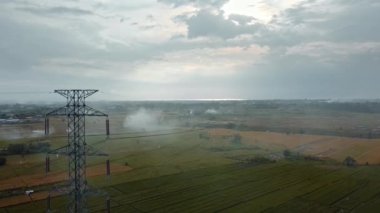 Gün batımında yeşil pirinç tarlasında yeni inşa edilmiş bir elektrik iletim kulesinin hava aracı görüntüsü.