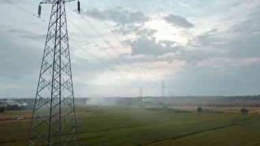 Gün batımında yeşil pirinç tarlasında yeni inşa edilmiş bir elektrik iletim kulesinin hava aracı görüntüsü.
