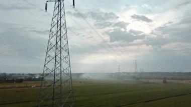 Gün batımında yeşil pirinç tarlasında yeni inşa edilmiş bir elektrik iletim kulesinin hava aracı görüntüsü.