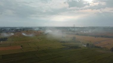 Gün batımında yeşil pirinç tarlasında yeni inşa edilmiş bir elektrik iletim kulesinin hava aracı görüntüsü.