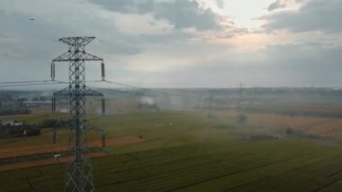 Gün batımında yeşil pirinç tarlasında yeni inşa edilmiş bir elektrik iletim kulesinin hava aracı görüntüsü.