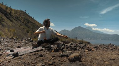 Tibedt çalan genç bir Asyalı doğadaki bir dağda bakır bardaklar söylüyor.