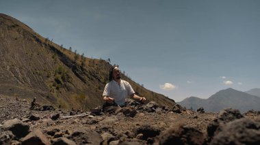 Tibedt çalan genç bir Asyalı doğadaki bir dağda bakır bardaklar söylüyor.