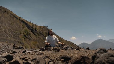 Tibedt çalan genç bir Asyalı doğadaki bir dağda bakır bardaklar söylüyor.