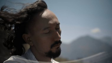 Tibedt çalan genç bir Asyalı doğadaki bir dağda bakır bardaklar söylüyor.