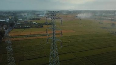 Gün batımında yeşil pirinç tarlasında yeni inşa edilmiş bir elektrik iletim kulesinin hava aracı görüntüsü.