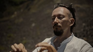 Tibedt çalan genç bir Asyalı doğadaki bir dağda bakır bardaklar söylüyor.