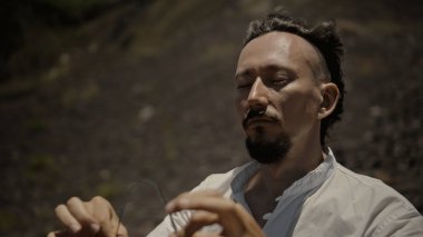 Tibedt çalan genç bir Asyalı doğadaki bir dağda bakır bardaklar söylüyor.