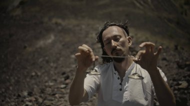 Tibedt çalan genç bir Asyalı doğadaki bir dağda bakır bardaklar söylüyor.