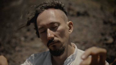 Tibedt çalan genç bir Asyalı doğadaki bir dağda bakır bardaklar söylüyor.