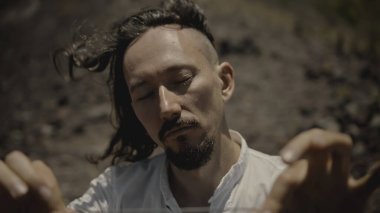 Tibedt çalan genç bir Asyalı doğadaki bir dağda bakır bardaklar söylüyor.