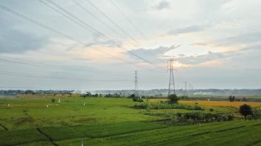 Gün batımında yeşil pirinç tarlasında yeni inşa edilmiş bir elektrik iletim kulesinin hava aracı görüntüsü.