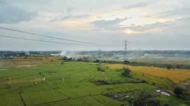 Gün batımında yeşil pirinç tarlasında yeni inşa edilmiş bir elektrik iletim kulesinin hava aracı görüntüsü.