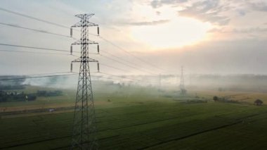 Gün batımında yeşil pirinç tarlasında yeni inşa edilmiş bir elektrik iletim kulesinin hava aracı görüntüsü.