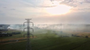 Gün batımında yeşil pirinç tarlasında yeni inşa edilmiş bir elektrik iletim kulesinin hava aracı görüntüsü.