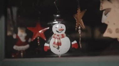 Küçük beyaz Noel oyuncakları. Kardan adamlar evdeki camın arkasında bir ipliğe tutunuyorlar.