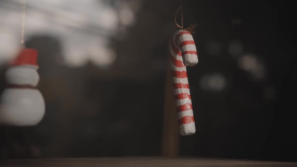 家の中のガラスの後ろの糸に吊るされた小さな白と赤のクリスマスの飾りの杖 — ストック動画