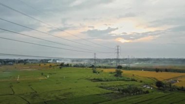 Gün batımında yeşil pirinç tarlasında yeni inşa edilmiş bir elektrik iletim kulesinin hava aracı görüntüsü.