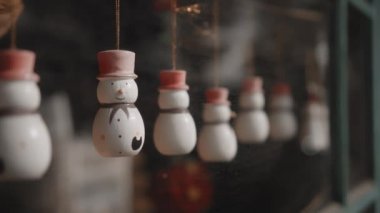 Küçük beyaz Noel oyuncakları. Kardan adamlar evdeki camın arkasında bir ipliğe tutunuyorlar.