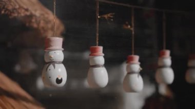 Küçük beyaz Noel oyuncakları. Kardan adamlar evdeki camın arkasında bir ipliğe tutunuyorlar.