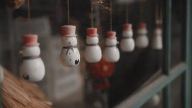 Küçük beyaz Noel oyuncakları. Kardan adamlar evdeki camın arkasında bir ipliğe tutunuyorlar.