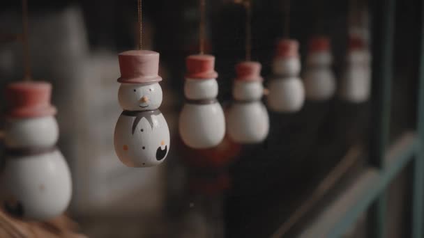 小さな白いクリスマスのおもちゃ雪だるまは家の中のガラスの後ろの糸にかかっています — ストック動画