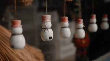 Küçük beyaz Noel oyuncakları. Kardan adamlar evdeki camın arkasında bir ipliğe tutunuyorlar.