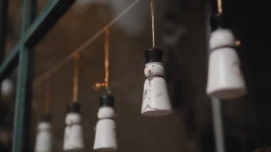 Küçük beyaz Noel oyuncakları. Kardan adamlar evdeki camın arkasında bir ipliğe tutunuyorlar.