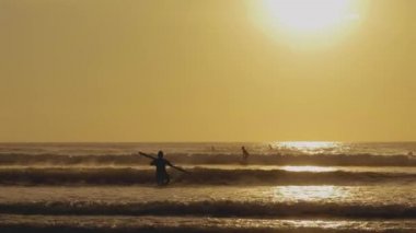 Gün batımında elinde kürekle sörf yapan genç bir adamın silueti.
