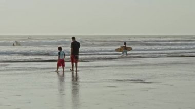 Kuta, Kabupaten Badung, Bali, Endonezya - 6 Kasım 2020: Genç baba koruyucu maskeler takmış çocuklarla sahilde yürüyor