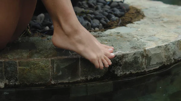 一位身穿泳衣的年轻漂亮的欧洲姑娘坐在游泳池边 一双光着脚的湿腿用手触摸着她的腿 — 图库照片
